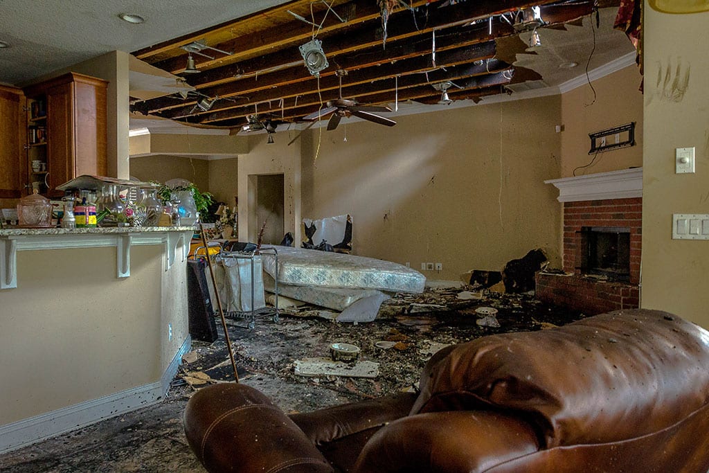 Fire damage restoration in NJ: fire-damaged living room with a collapsed ceiling and soot-covered furniture