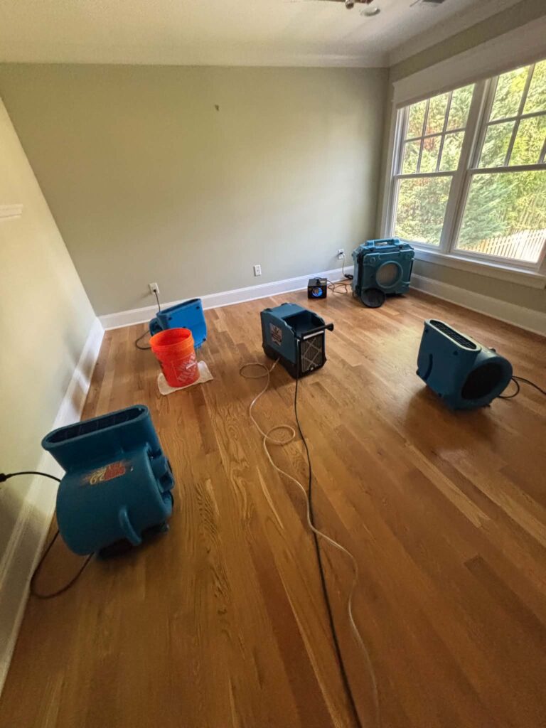 Air movers drying a water-damaged hardwood floor in an empty room